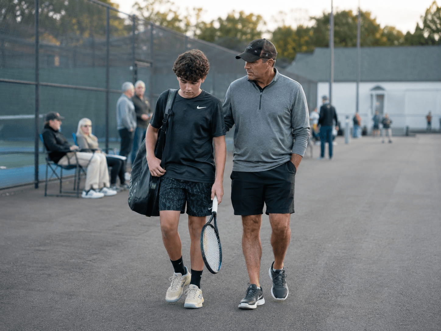 A parent and athlete talking beside the tennis court